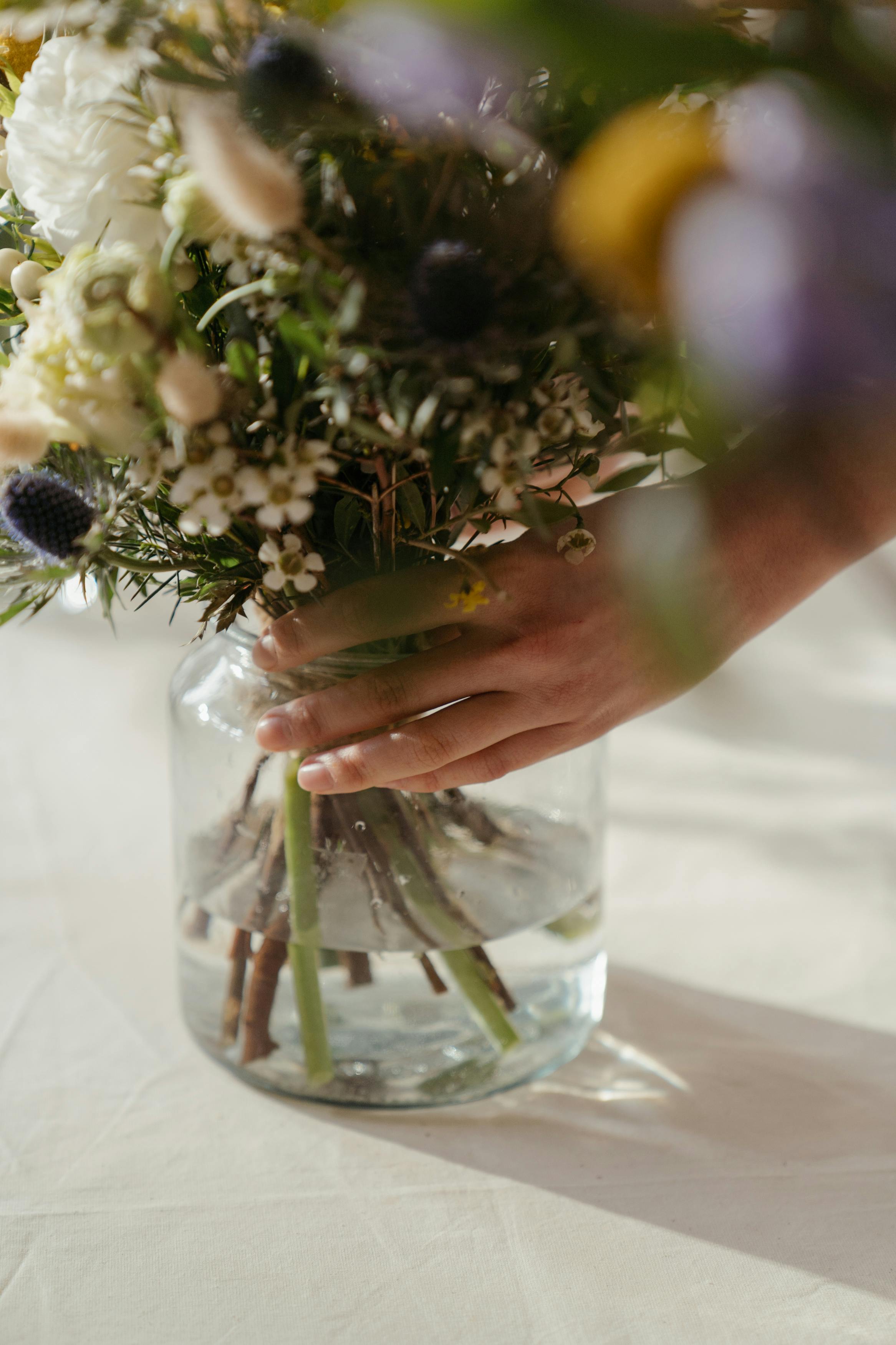 Flowers being arranged in a glass vase.